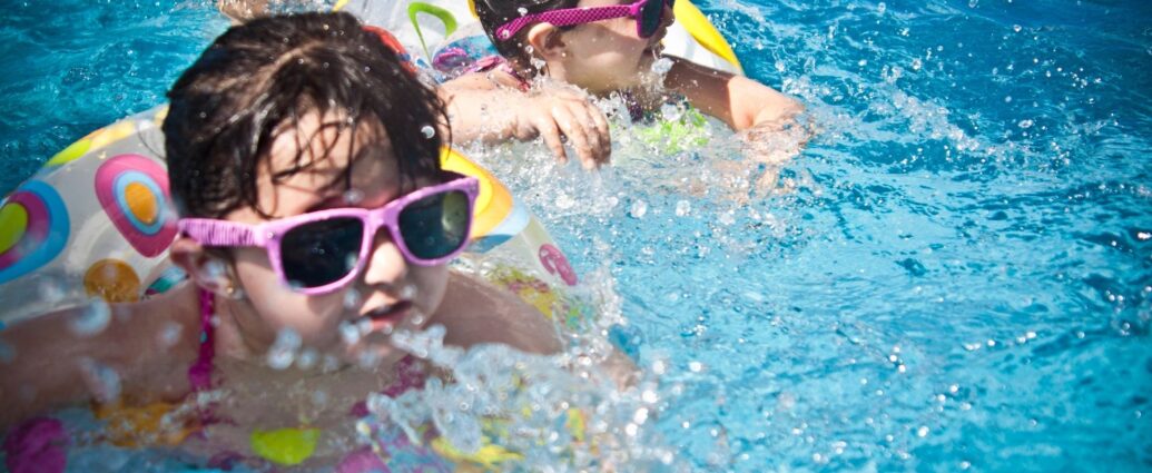 Two young girls in swimming pool with sunglasses and floats