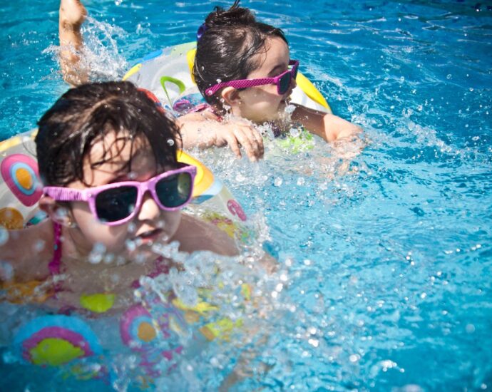 Two young girls in swimming pool with sunglasses and floats