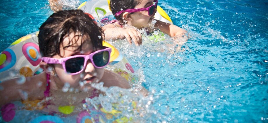 Two young girls in swimming pool with sunglasses and floats