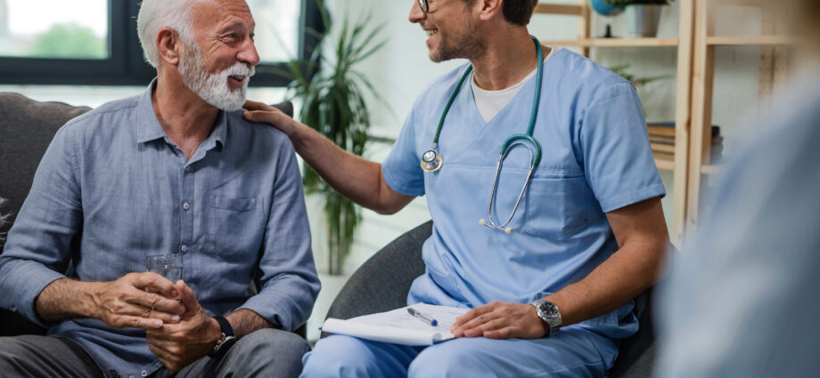 Happy doctor talking to senior male patient while being in a home visit.
